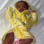 Jveion joined the competition — help win amazing prizes! baby, child, yellow_robe, bed, white_bedspread, foot, face, curly_hair, infant, cute, lying_down, cozy, blanket, diaper, sleepwear, indoors, soft_fabric, smiling, skin, hooded_clothing