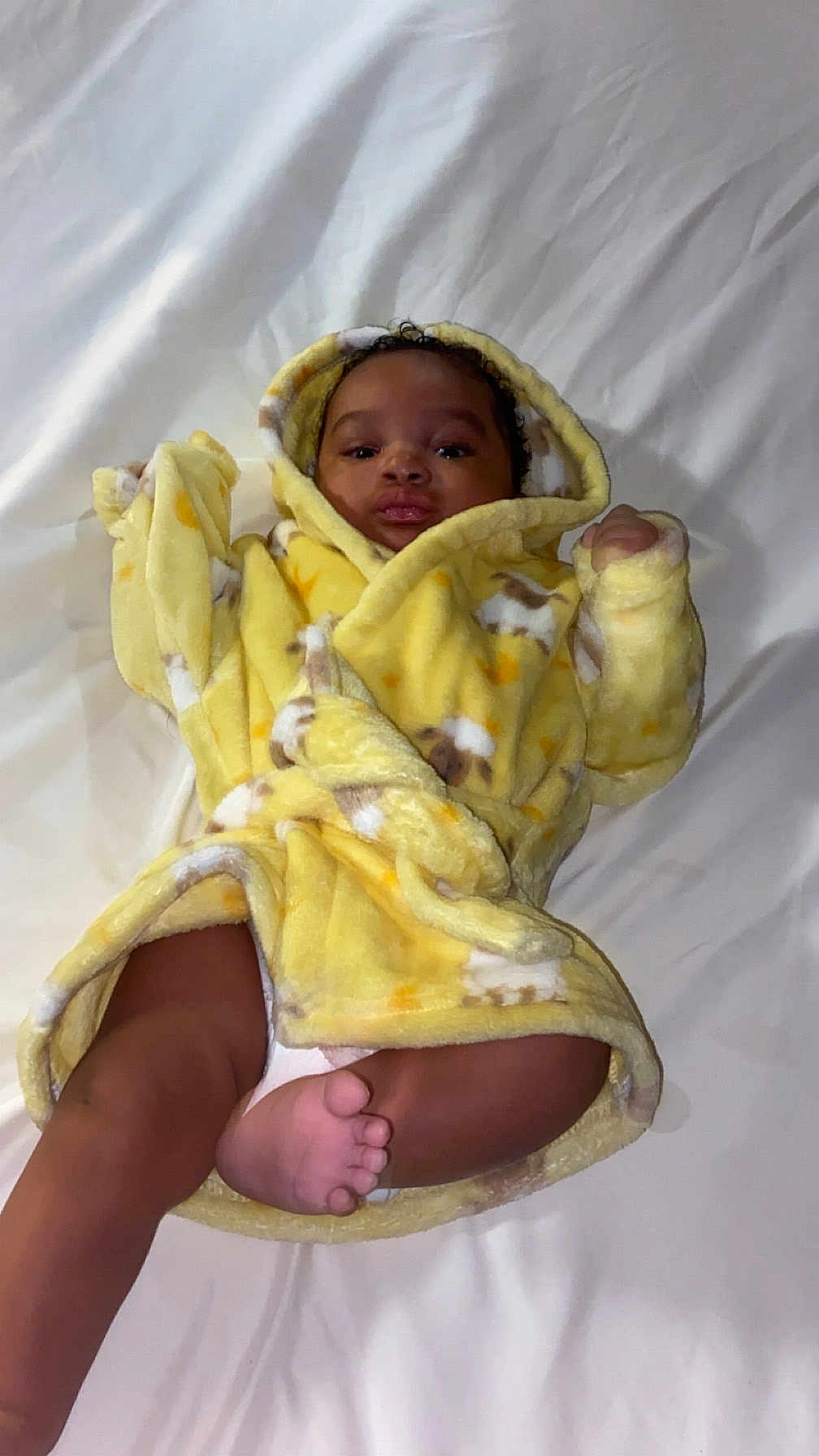Jveion joined the competition — help win amazing prizes! baby, child, yellow_robe, bed, white_bedspread, foot, face, curly_hair, infant, cute, lying_down, cozy, blanket, diaper, sleepwear, indoors, soft_fabric, smiling, skin, hooded_clothing