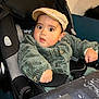 baby, child, car_seat, cap, green_jacket, wide_eyes, curious, indoor, table, clothing, person, seat_belt, face, headwear, infant, expression, furniture, cute, portrait, young_child