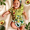 baby, infant, child, smiling, avocado, fruit, green_leaves, blanket, clothing, headband, cute, lying_down, happy, portrait, toddler, nature, fresh, soft_texture, playful, outdoor_style