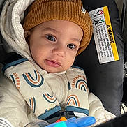 Zyon joined the competition — help win amazing prizes! baby, child, car_seat, hat, knit_hat, jacket, rainbow_pattern, toy, blue_toy, infant, closeup, face, eyes, cute, warm_clothing, seatbelt, car, portrait, indoor, child_safety