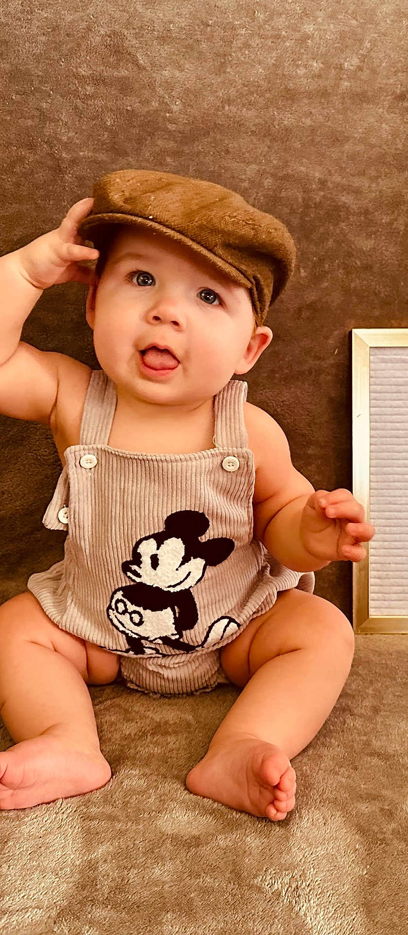 Greyson joined the competition — help win amazing prizes! baby, child, infant, cap, hat, romper, mickey_mouse, tongue_out, cute, sitting, soft_texture, brown, playful, chubby_cheeks, indoors, portrait, happy, clothing, person, face