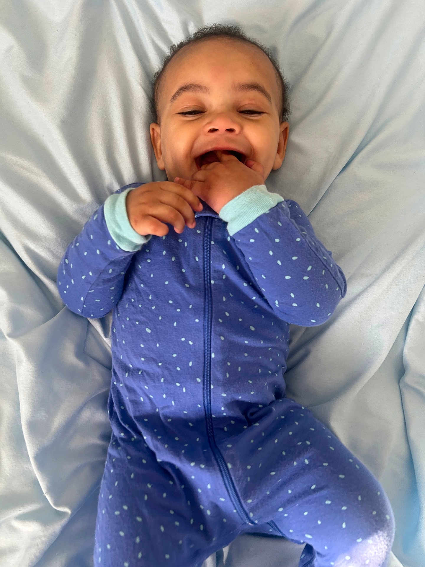 Ashure Matthews joined the competition — help win amazing prizes! baby, child, infant, onesie, blue_clothing, polka_dot, smiling, happy, lying_down, blanket, bed, cute, hands, fingers, mouth, face, skin, hair, indoors, soft