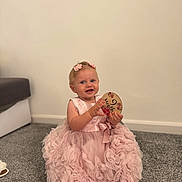 Evelyn joined the competition — help win amazing prizes! child, baby, girl, pink_dress, flower_clips, carpet, indoor, smiling, holding_object, footwear, sitting, cute, decorative_sign, happy, portrait, head, person, floor, wall, home
