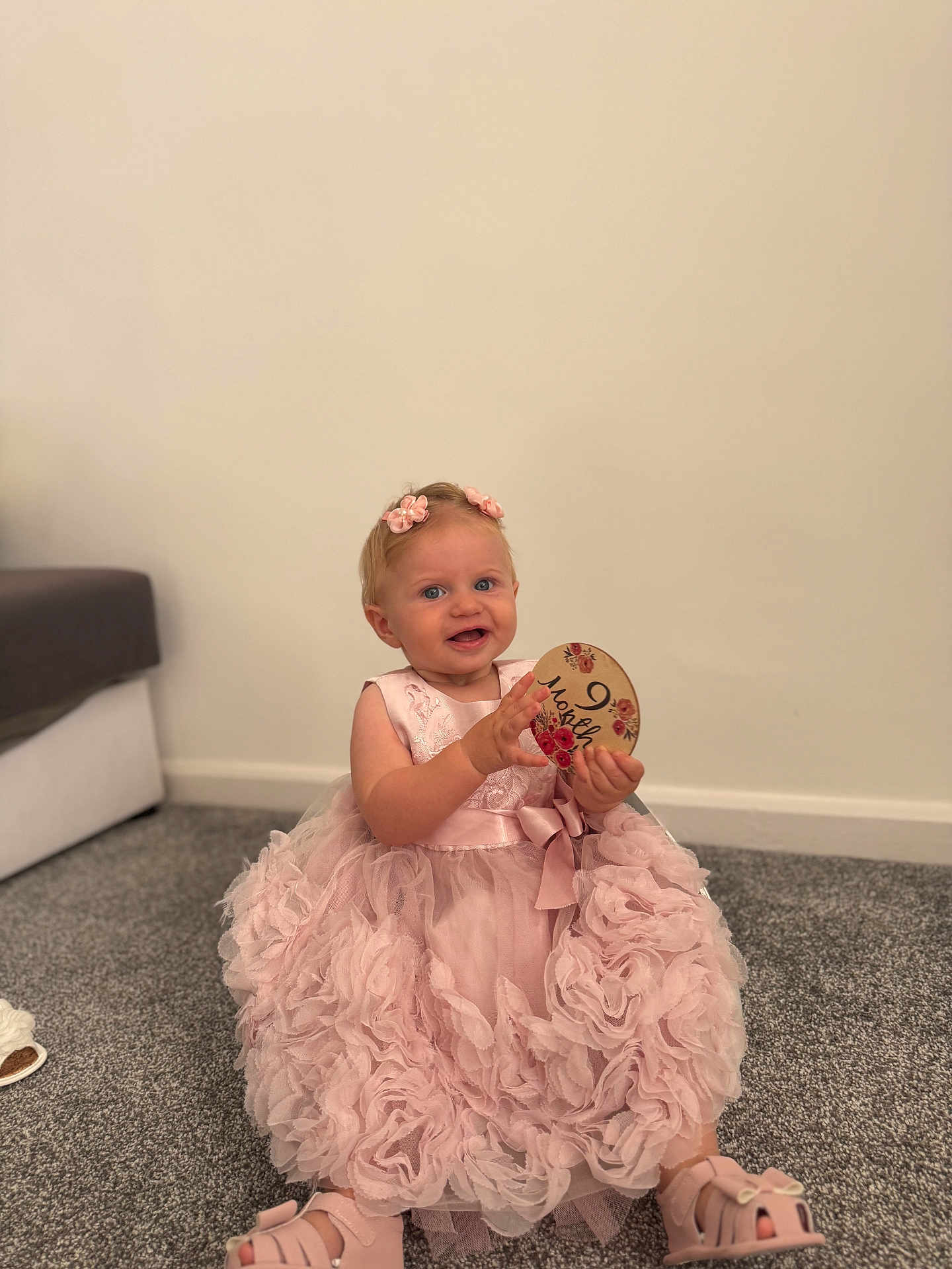Evelyn joined the competition — help win amazing prizes! child, baby, girl, pink_dress, flower_clips, carpet, indoor, smiling, holding_object, footwear, sitting, cute, decorative_sign, happy, portrait, head, person, floor, wall, home
