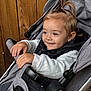 toddler, child, stroller, smiling, happy, clothing, white_sweater, black_vest, pony_tail, hands, wooden_background, seat, baby, person, outdoor, casual, portrait, infant, cute, comfort