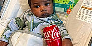 Yani is registered to the contest to win money with this photo: baby, baby_rocker, child, clothing, coca_cola_can, colorful, cute, dinosaur_onesie, drink_can, giraffe, holding, indoor, infant, jungle_animals, portrait, seat, sloth, toddler, toucan, toy_pattern