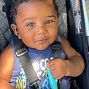 Yani joined the competition — help win amazing prizes! baby, child, smiling, stroller, seatbelt, toy, curly_hair, blue_shirt, red_shorts, closeup, infant, cute, happy, sitting, outdoor, sunlight, black_hair, person, portrait, baby_toy