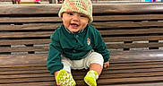 Elijah joined the competition — help win amazing prizes! baby, child, smiling, bench, hat, green_jacket, socks, wooden_bench, urban, brick_wall, shop_window, happy, cute, portrait, seated, outdoor, infant, casual, colorful, playful
