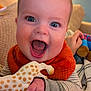 baby, smiling, blue_eyes, toy, giraffe, hand, orange_bib, striped_clothing, couch, blanket, indoor, happy, face, infant, cheerful, close_up, child, person, comfort, warm_lighting