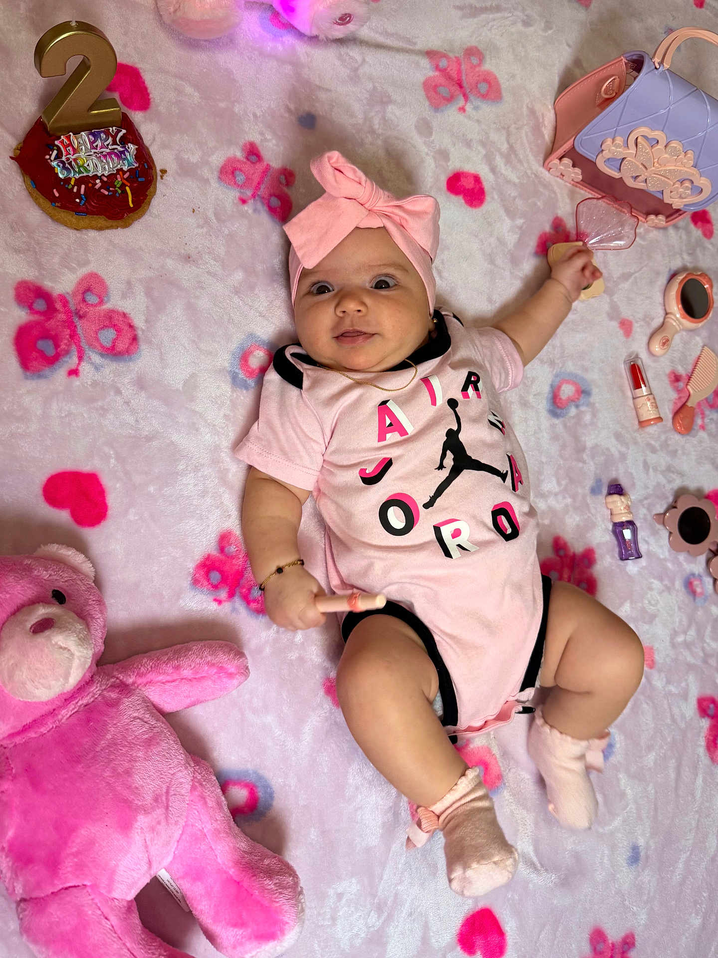Fernanda is registered to the contest to win money with this photo: baby, girl, pink, headband, onesie, blanket, toy, stuffed_animal, birthday, cupcake, candle, butterfly_pattern, sock, smile, face, laying, cute, infant, play, happy