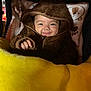 Aylani is registered to the contest to win money with this photo: baby, child, smiling, hooded_clothing, blanket, yellow_blanket, pink_pillow, cozy, cute, infant, portrait, indoor, warm, soft_texture, face, hand, happy, person, baby_clothes, sleeping_bag
