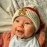 Olivia participe au concours pour gagner de l'argent avec cette photo : baby, infant, knitted_hat, gingerbread_patch, smile, tongue_out, blue_eyes, cheeks, bib, blanket, plush_texture, fur_blanket, cozy, portrait, close_up, laying_down, happy, cute, warm_clothing, indoor