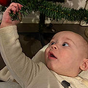 Maëlo a rejoint le concours — aidez-le/la à gagner de superbes lots ! baby, blue_eyes, celebration, child, christmas_tree, closeup, clothing, curiosity, decorations, expression, face, festive, hand, holiday, indoor, infant, ornament, seasonal, sleeve, tree_branch
