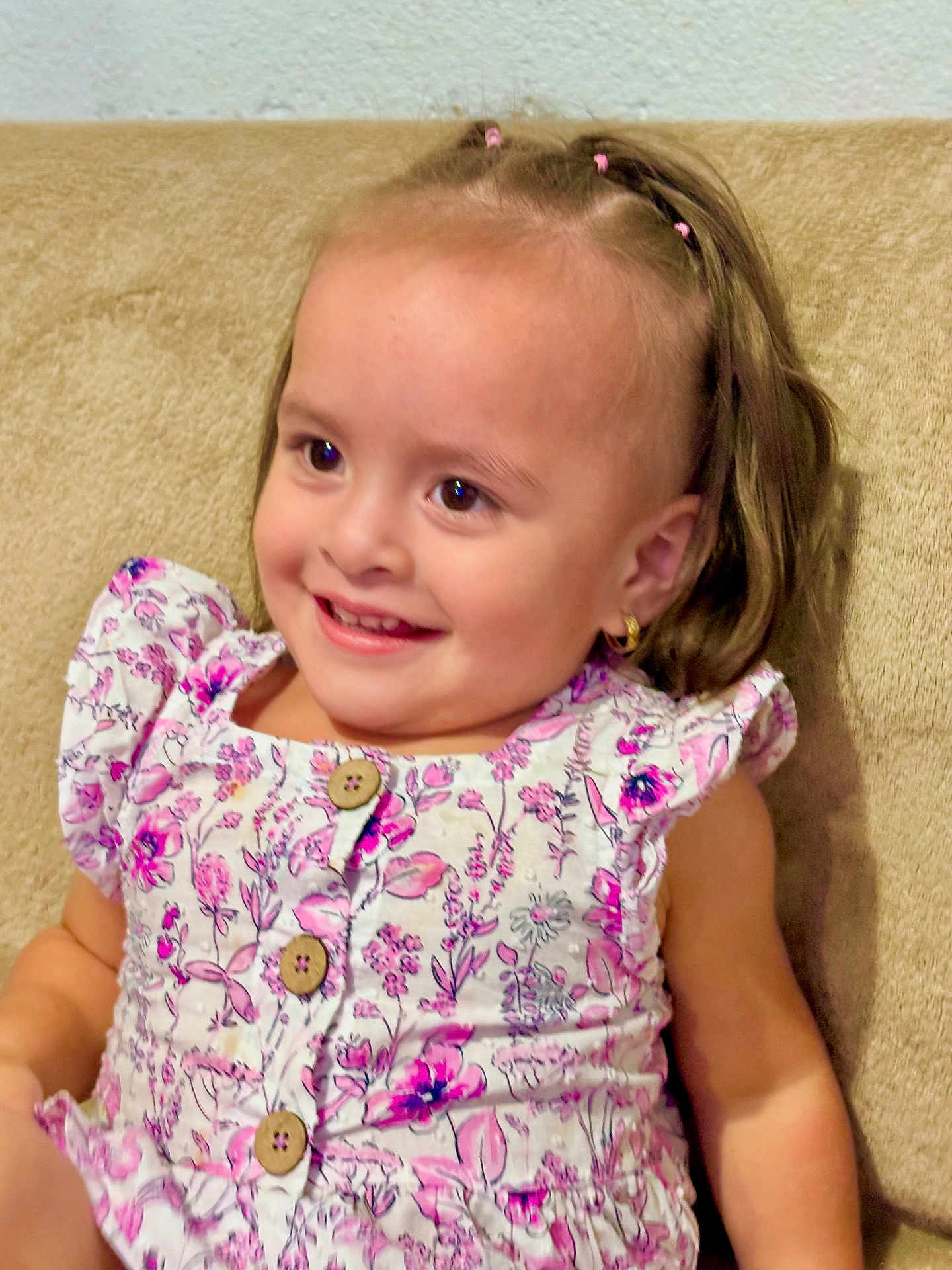 Mila joined the competition — help win amazing prizes! child, toddler, smiling, girl, floral_dress, pink, hair_ties, earrings, couch, indoor, portrait, happy, cute, seated, young_child, apparel, buttoned_dress, skin, face, person