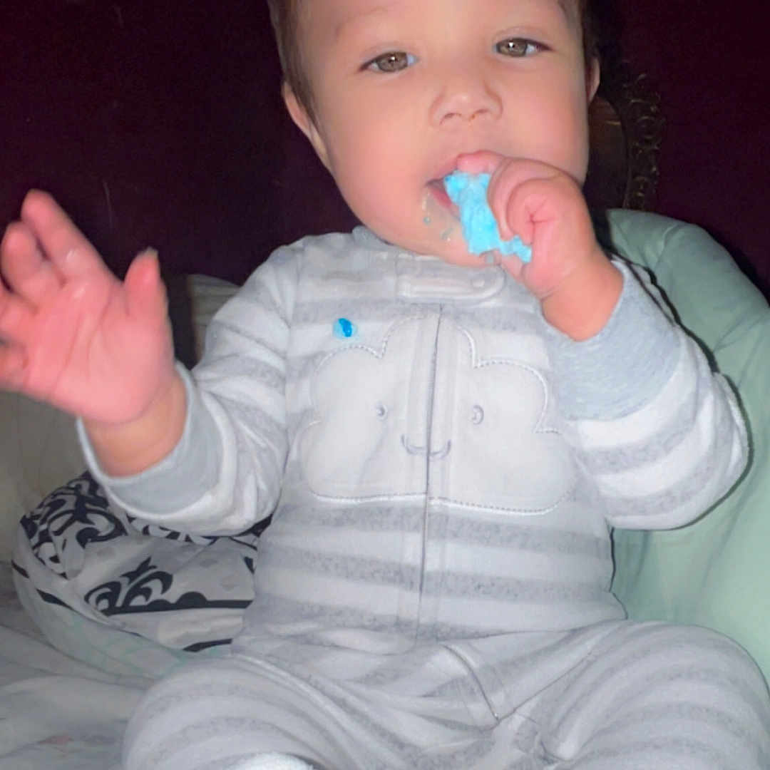 Christian joined the competition — help win amazing prizes! baby, child, pajamas, striped_clothing, bed, indoor, person, face, hand, sitting, cute, snack, chewing, blue_food, infant, young_child, cozy, sleepwear, smiling, portrait