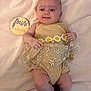 Adelina is registered to the contest to win money with this photo: baby, infant, child, yellow_outfit, daisy, flower_pattern, blanket, soft_fabric, wooden_sign, smile, lying_down, cute, skin, person, baby_socks, infant_clothing, portrait, indoors, young_child, four_months