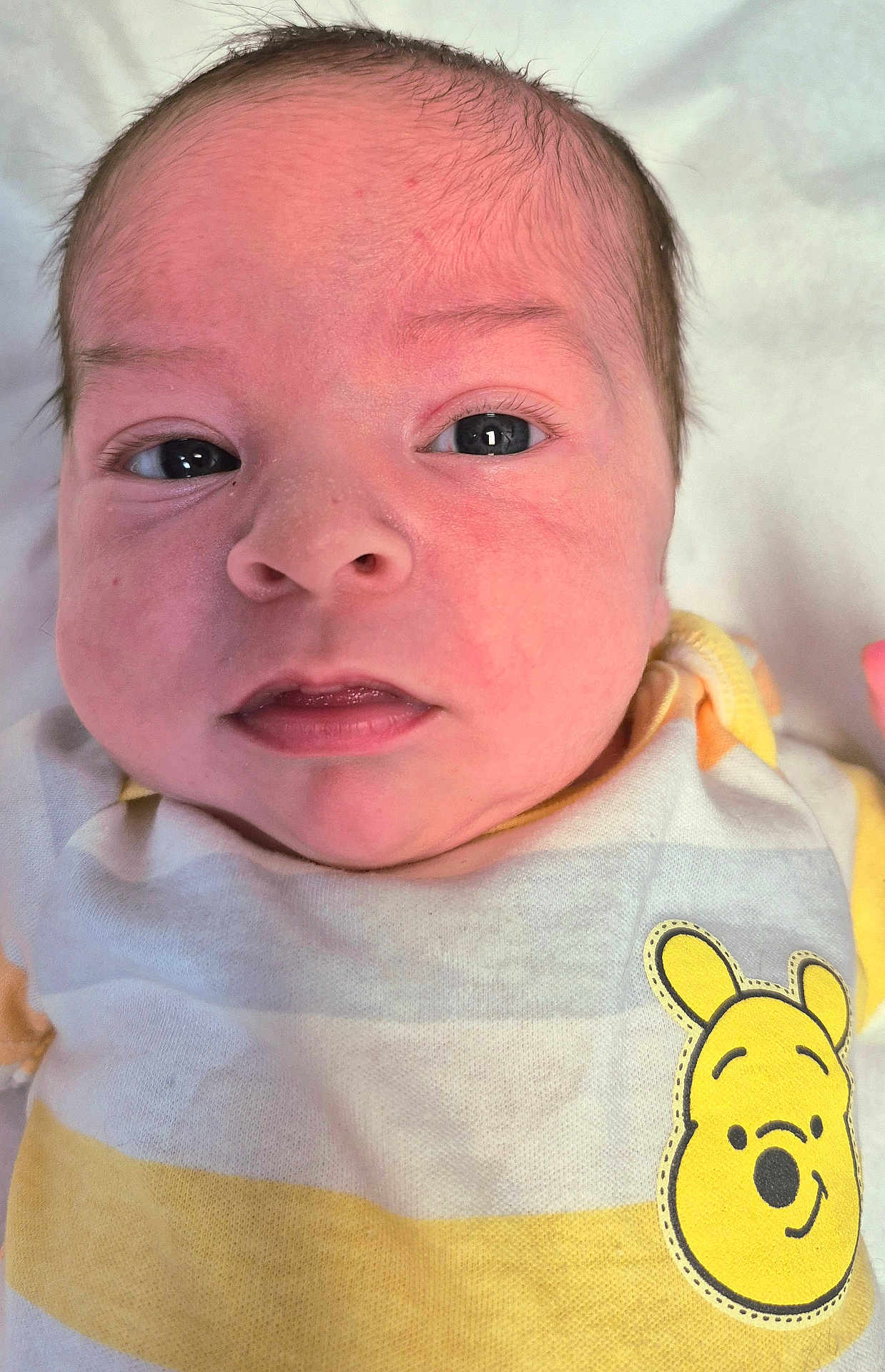 Braxton is registered to the contest to win money with this photo: baby, newborn, face, closeup, infant, eyes, mouth, skin, clothing, yellow, white, cute, portrait, lying_down, soft, baby_outfit, patch, expression, head, child