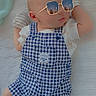 baby, infant, blue_checkered_overalls, mittens, white_blanket, sunglasses, reflection, cityscape, cute, sleeping, child, portrait, laying_down, soft_texture, fashion, indoors, peaceful, small_hands, comfortable, adorable