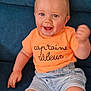 baby, child, smiling, blue_eyes, orange_tshirt, denim_shorts, sitting, couch, indoor, happy, face, person, toddler, shorts, clothing, fist_pump, hair, cute, casual, playful