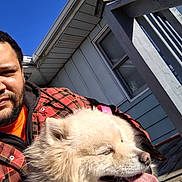 Prada joined the competition — help win amazing prizes! person, dog, porch, house, window, railing, sky, blue_sky, sunlight, tongue, fur, smile, beard, flannel_jacket, plaid, jeans, sitting, pet, outdoor, front_porch