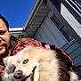 Prada is registered to the contest to win money with this photo: man, bearded_man, dog, fluffy_dog, blue_eyes, tongue_out, smiling_dog, leash, harness, outdoor, house, porch, railing, clear_sky, sunny, plaid_shirt, selfie, close_up, white_fur, pet_owner