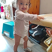 Lana a rejoint le concours — aidez-le/la à gagner de superbes lots ! toddler, child, smiling, indoors, pigtails, white_shirt, socks, standing, table, high_chair, step_stool, wooden_floor, cabinet, toy, hand, furniture, room, happy, curly_hair, person