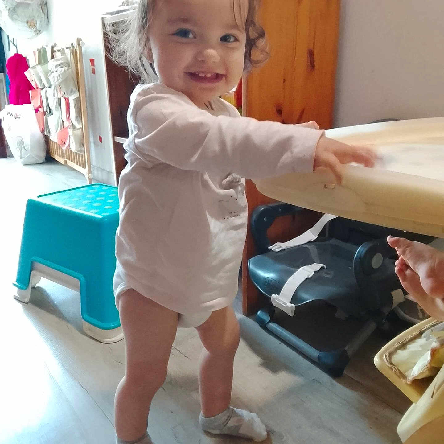 Lana a rejoint le concours — aidez-le/la à gagner de superbes lots ! toddler, child, smiling, indoors, pigtails, white_shirt, socks, standing, table, high_chair, step_stool, wooden_floor, cabinet, toy, hand, furniture, room, happy, curly_hair, person