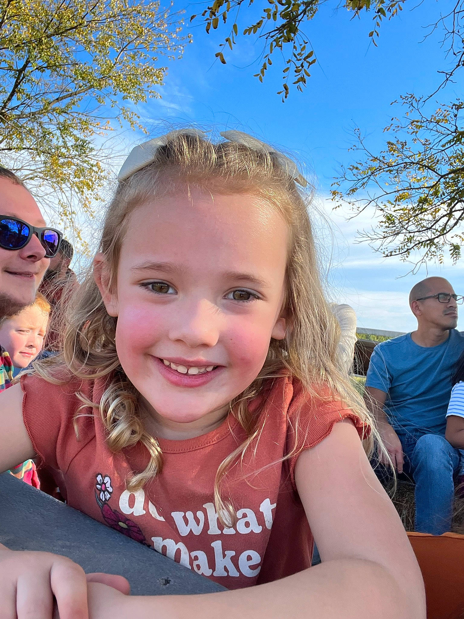 Macy is registered to the contest to win money with this photo: blue, event, face, facial_expression, fun, gesture, goggles, grass, happy, joy, leisure, people_in_nature, person, recreation, skin, sky, smile, sunglasses, t_shirt, toddler