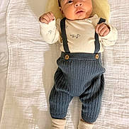 Endrick Palacios is registered to the contest to win money with this photo: baby, infant, blanket, plush, pillow, knitted_pants, suspenders, socks, clothing, person, face, cute, lying_down, indoors, soft_texture, baby_garment, newborn, portrait, expression, child