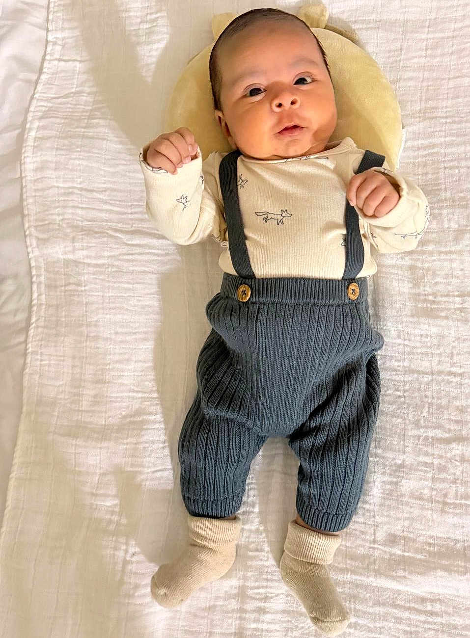 Endrick Palacios is registered to the contest to win money with this photo: baby, infant, blanket, plush, pillow, knitted_pants, suspenders, socks, clothing, person, face, cute, lying_down, indoors, soft_texture, baby_garment, newborn, portrait, expression, child