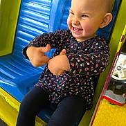 Meli a rejoint le concours — aidez-le/la à gagner de superbes lots ! toddler, child, smiling, thumbs_up, playground, ride, colorful, blue_seat, yellow, floral_clothing, happy, cute, fun, outdoor, play, young_child, person, casual, joyful, expression