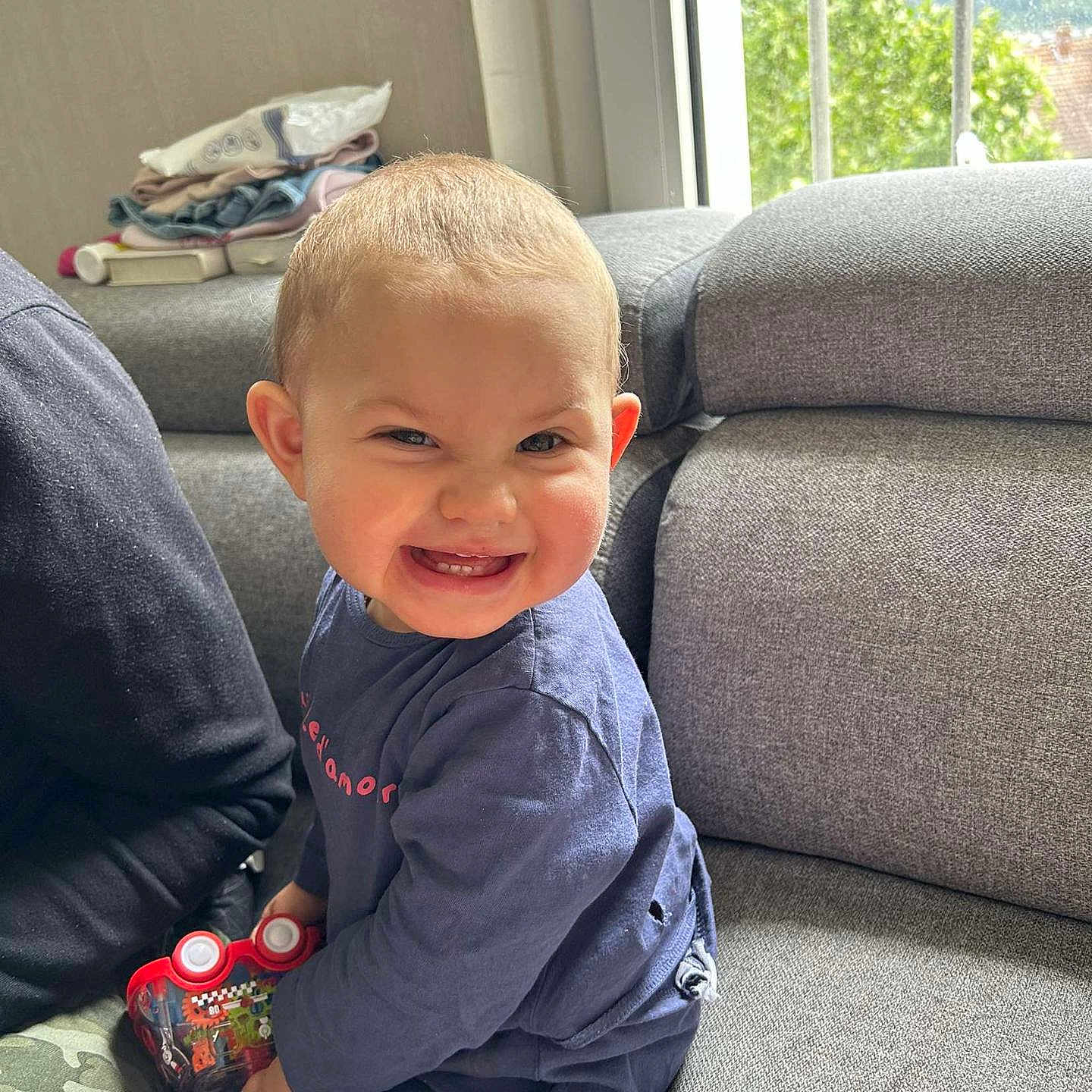 Meli a rejoint le concours — aidez-le/la à gagner de superbes lots ! casual_clothing, child, couch, daylight, expression, furniture, happy, home, indoor, living_room, person, playful, seated, short_hair, smiling, sofa, toddler, toy_car, window, young_child