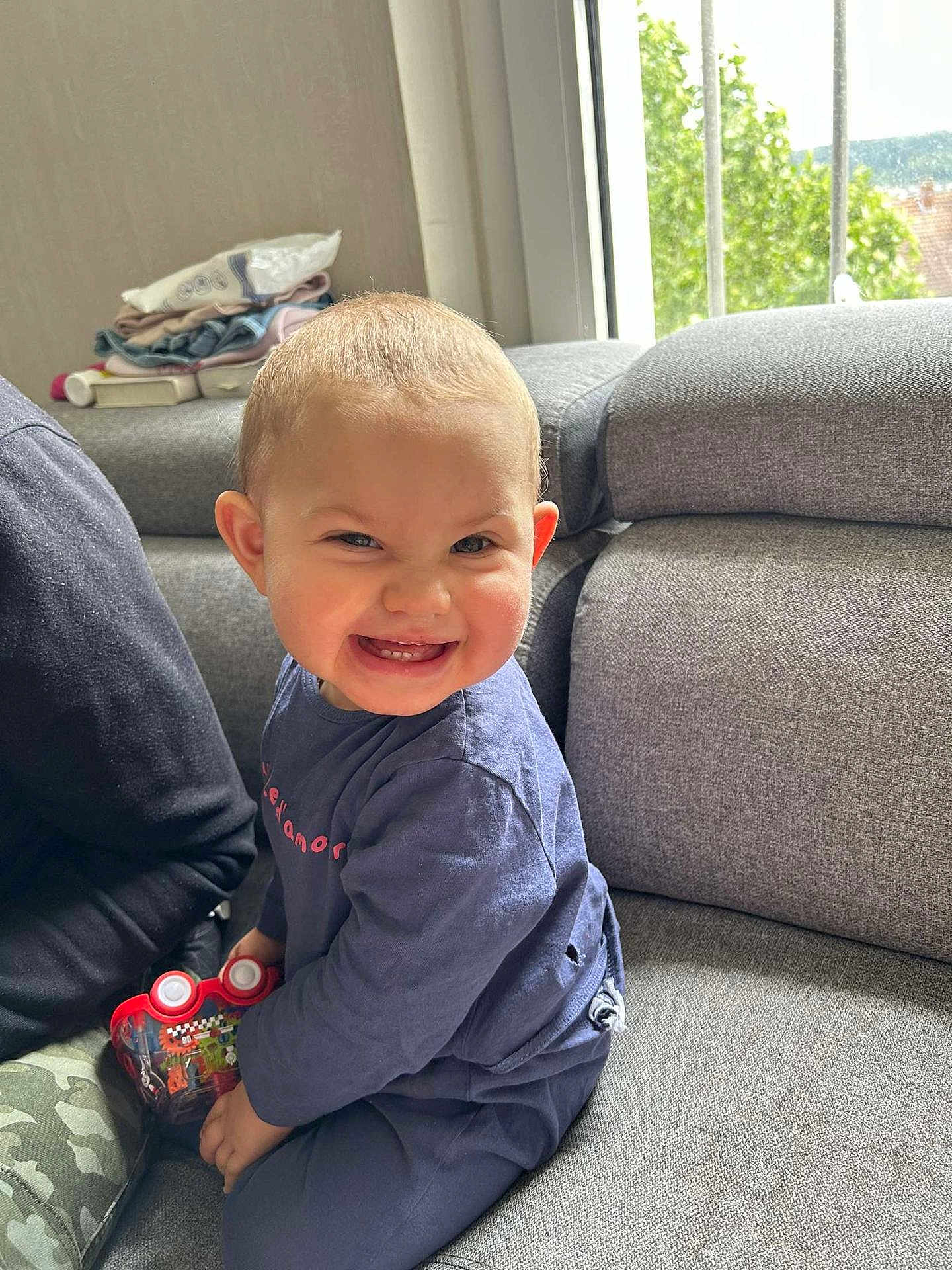 Meli a rejoint le concours — aidez-le/la à gagner de superbes lots ! toddler, child, smiling, toy_car, indoor, sofa, window, daylight, happy, casual_clothing, short_hair, couch, person, home, playful, seated, furniture, young_child, expression, living_room