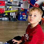 William participe au concours pour gagner de l'argent avec cette photo : blond_hair, blue_eyes, boy, candid, casual_clothing, child, curious_expression, floor_toys, hardwood_floor, indoor, playing, playroom, portrait, racecar_toy, red_sweatshirt, sitting, socks, toy_car, toy_racetrack, young_child
