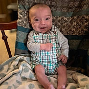 Brandon is registered to the contest to win money with this photo: baby, child, smiling, indoor, blanket, plaid, clothing, sitting, happy, face, person, chair, pattern, cute, young, infant, apparel, portrait, comfort, cozy