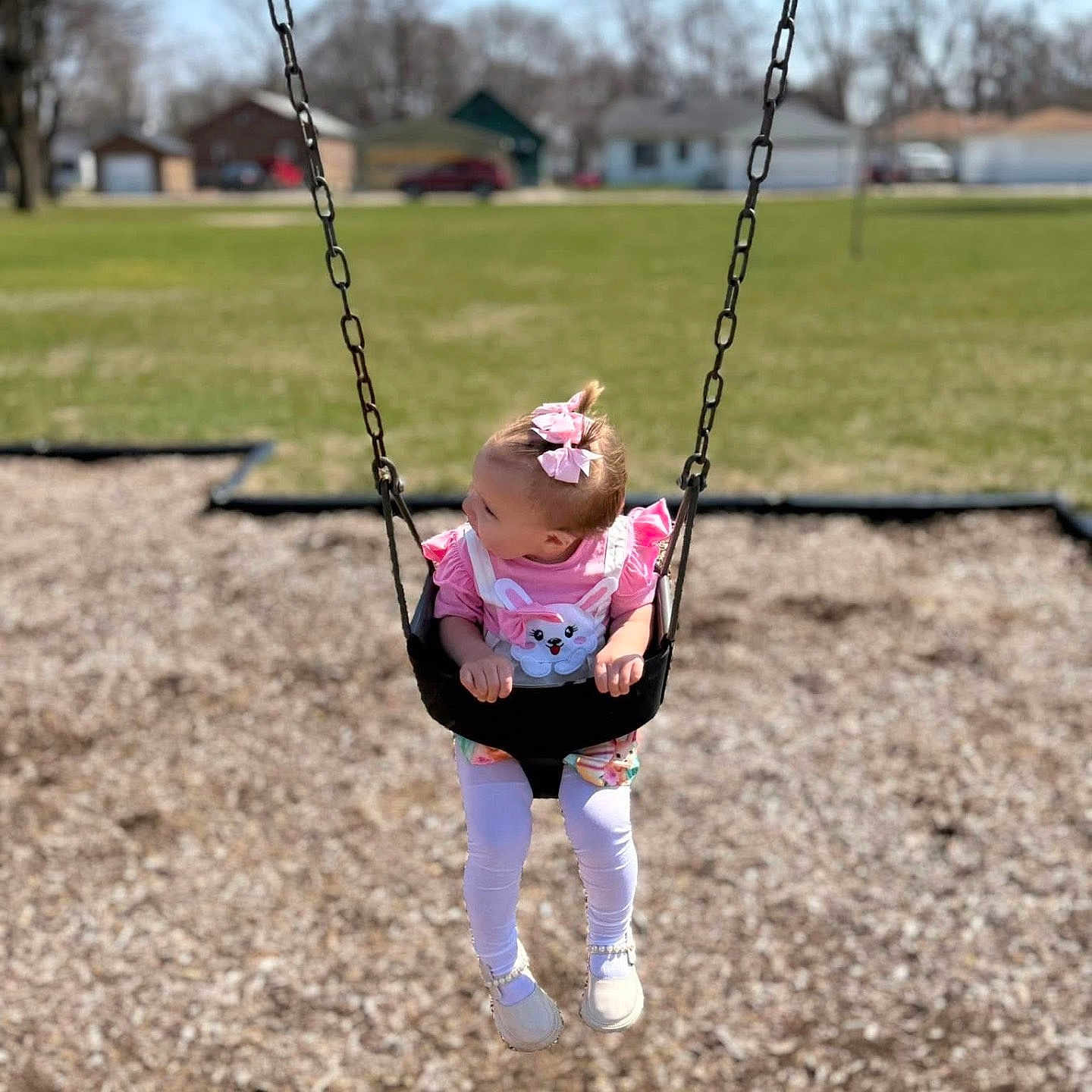 Rivhur is registered to the contest to win money with this photo: chains, child, curious, daylight, footwear, fun, grass, hair_bow, houses, legs, outdoor, park, person, pink_clothing, playground, summer, swing, toddler, white_shoes, woodchips