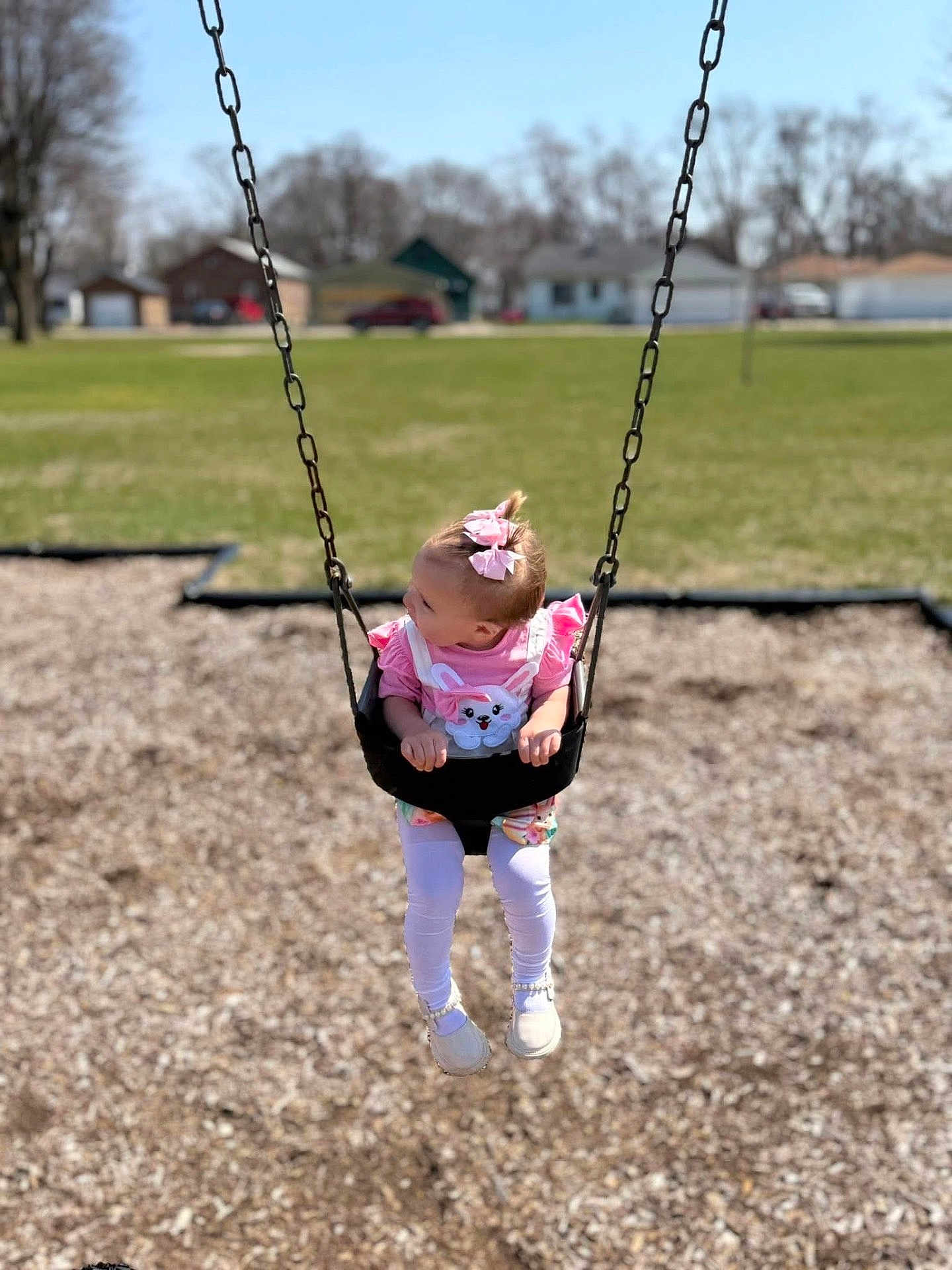 Rivhur is registered to the contest to win money with this photo: child, toddler, swing, playground, pink_clothing, hair_bow, outdoor, grass, houses, daylight, chains, footwear, white_shoes, legs, curious, person, woodchips, park, summer, fun
