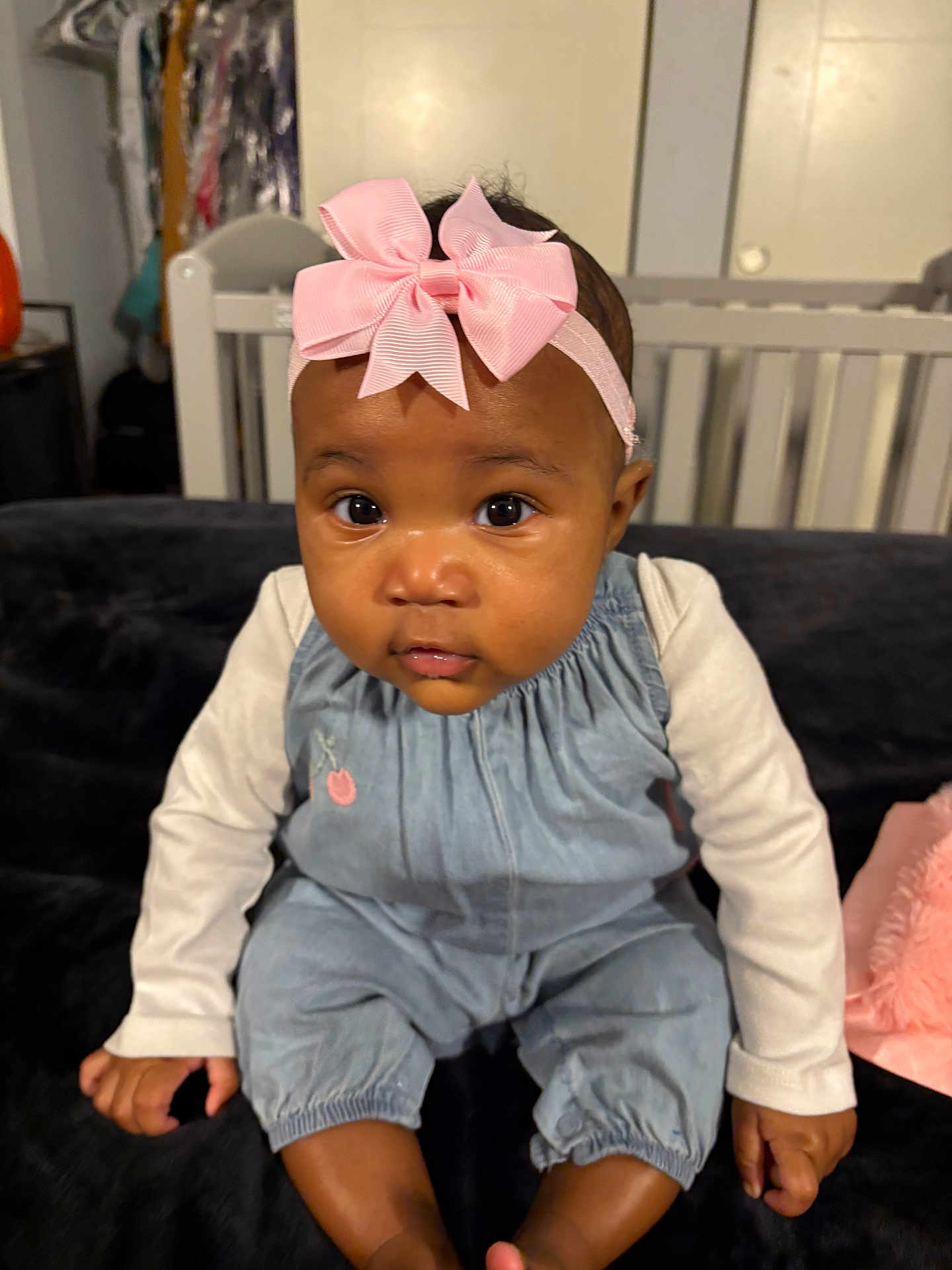 Zayah is registered to the contest to win money with this photo: baby, infant, child, headband, pink_bow, big_eyes, face, cheeks, onesie, denim_overall, long_sleeves, sitting, crib, couch, blanket, indoor, portrait, cute, hands, toes