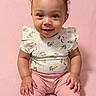 baby, child, smiling, pink_background, pink_pants, floral_top, bow, cute, portrait, sitting, infant, happy, face, person, studio, indoors, soft_lighting, young_child, toddler, fashion
