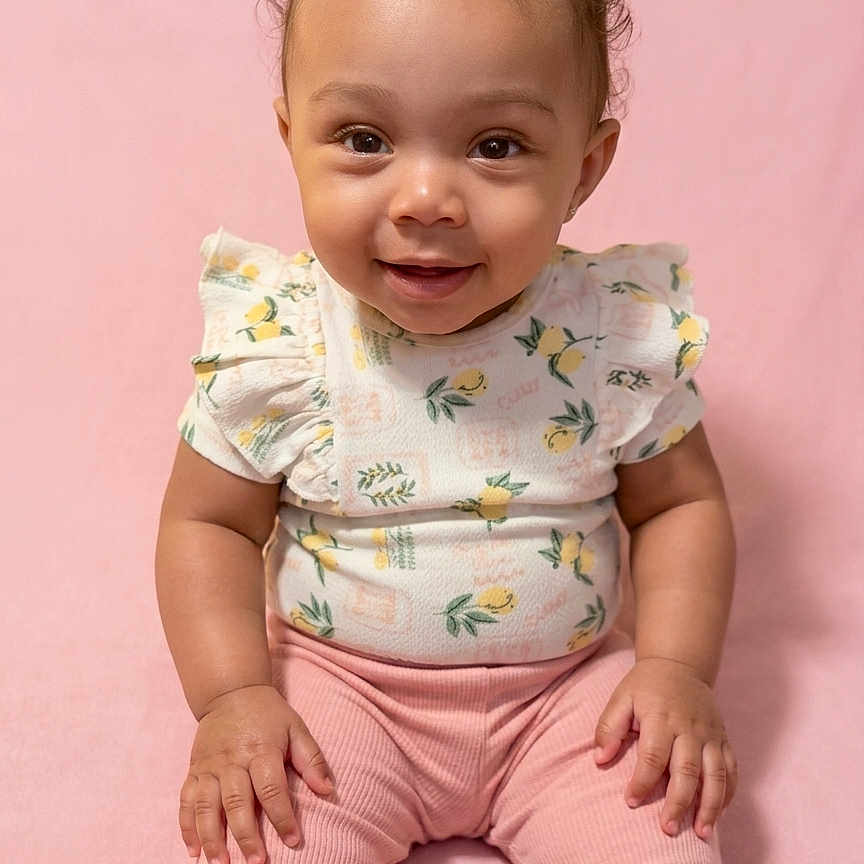 Sariyah joined the competition — help win amazing prizes! baby, child, smiling, pink_background, pink_pants, floral_top, bow, cute, portrait, sitting, infant, happy, face, person, studio, indoors, soft_lighting, young_child, toddler, fashion