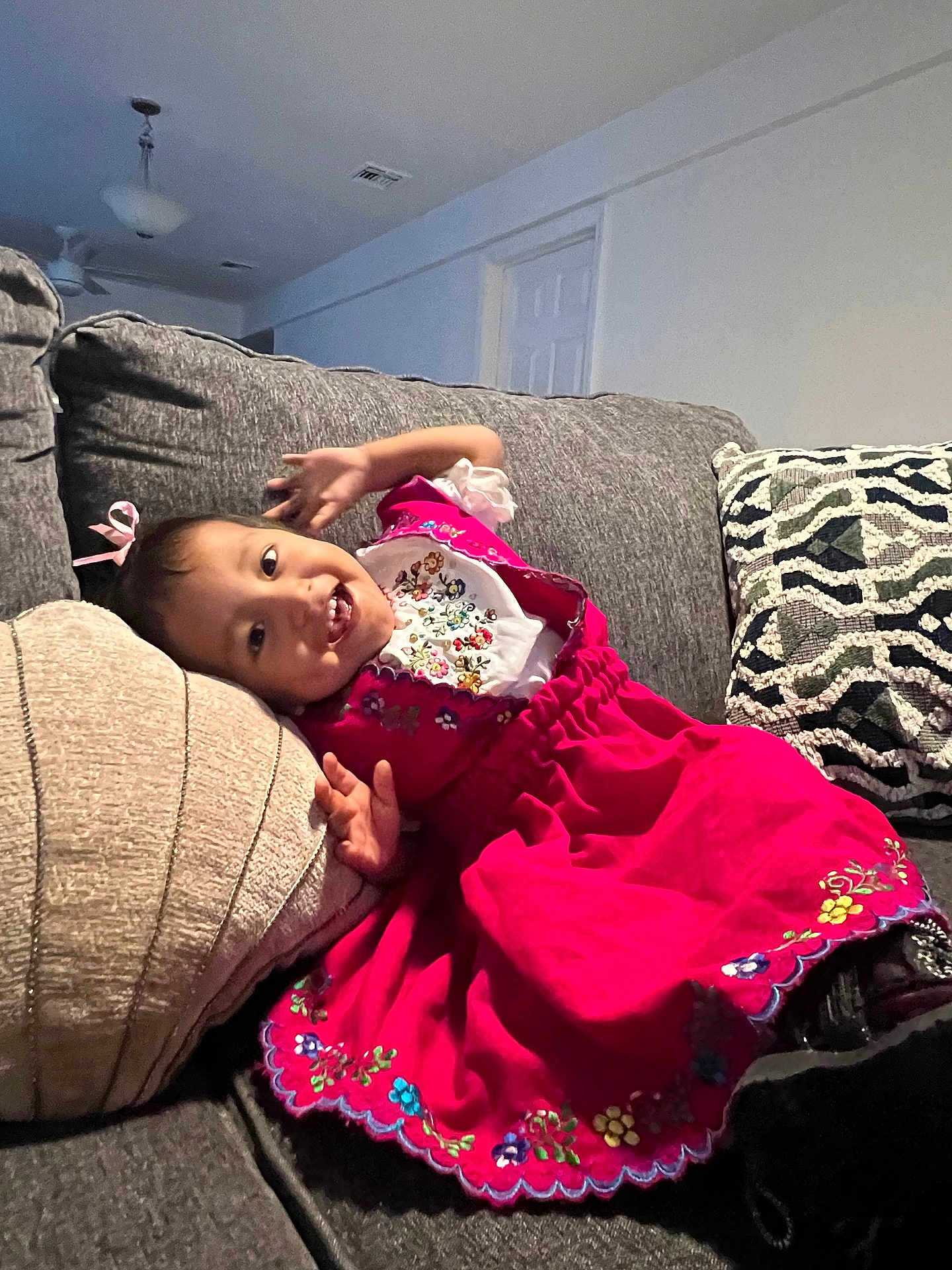 Daphne joined the competition — help win amazing prizes! toddler, child, smiling, dress, pink_dress, couch, pillow, indoor, happy, person, cute, embroidery, home, furniture, relaxed, fun, portrait, sitting, cozy, playful