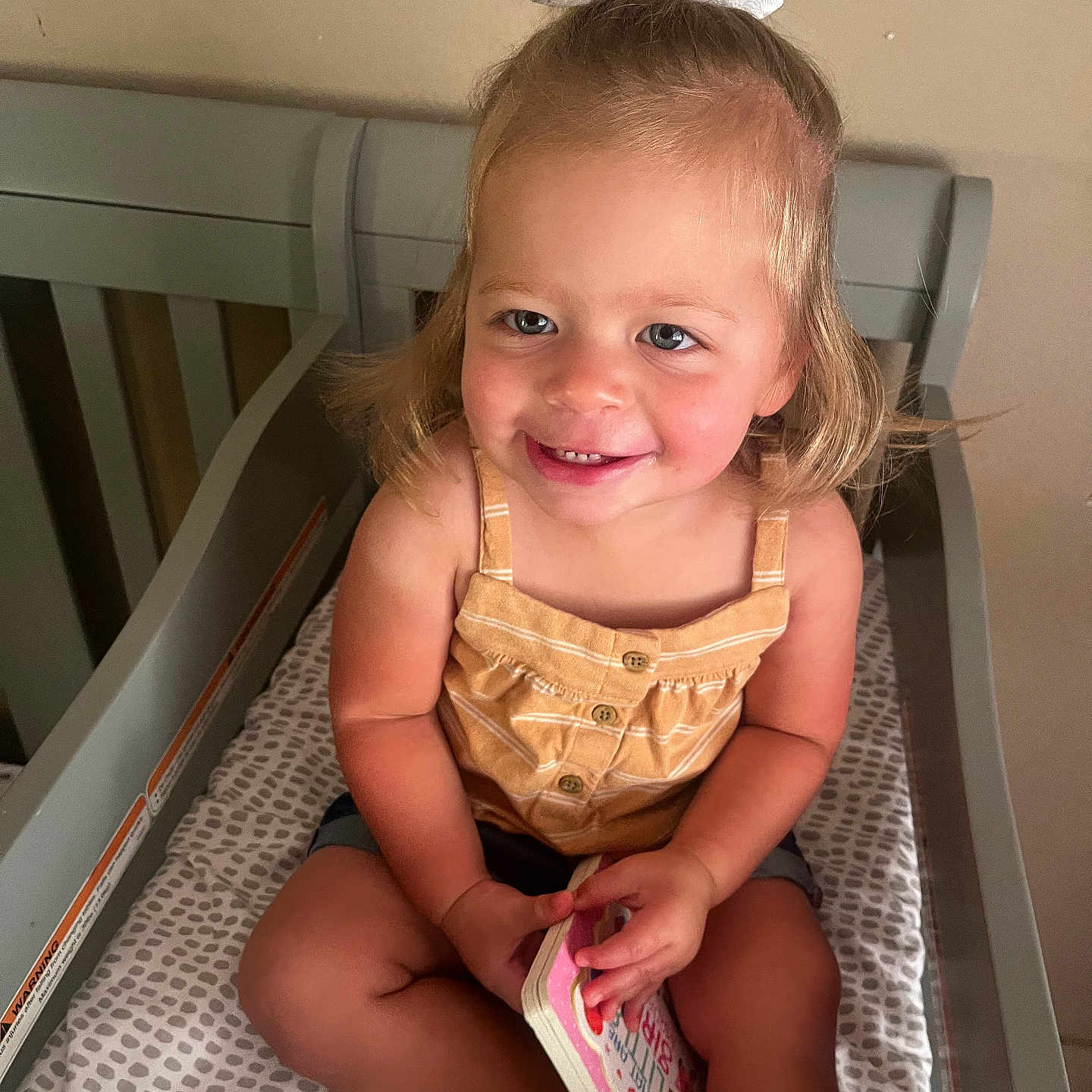 Lillian is registered to the contest to win money with this photo: bed, bodypart, child, crib, face, female, finger, furniture, girl, hand, happy, head, homedecor, indoors, infantbed, person, photography, portrait, reading, smile