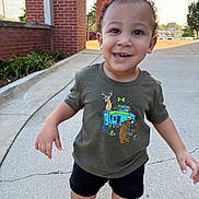 Zane is registered to the contest to win money with this photo: toddler, child, smiling, running, outdoor, curly_hair, tshirt, shorts, sidewalk, brick_wall, greenery, daytime, happy, person, casual_clothing, urban, young_child, playful, sunlight, footwear