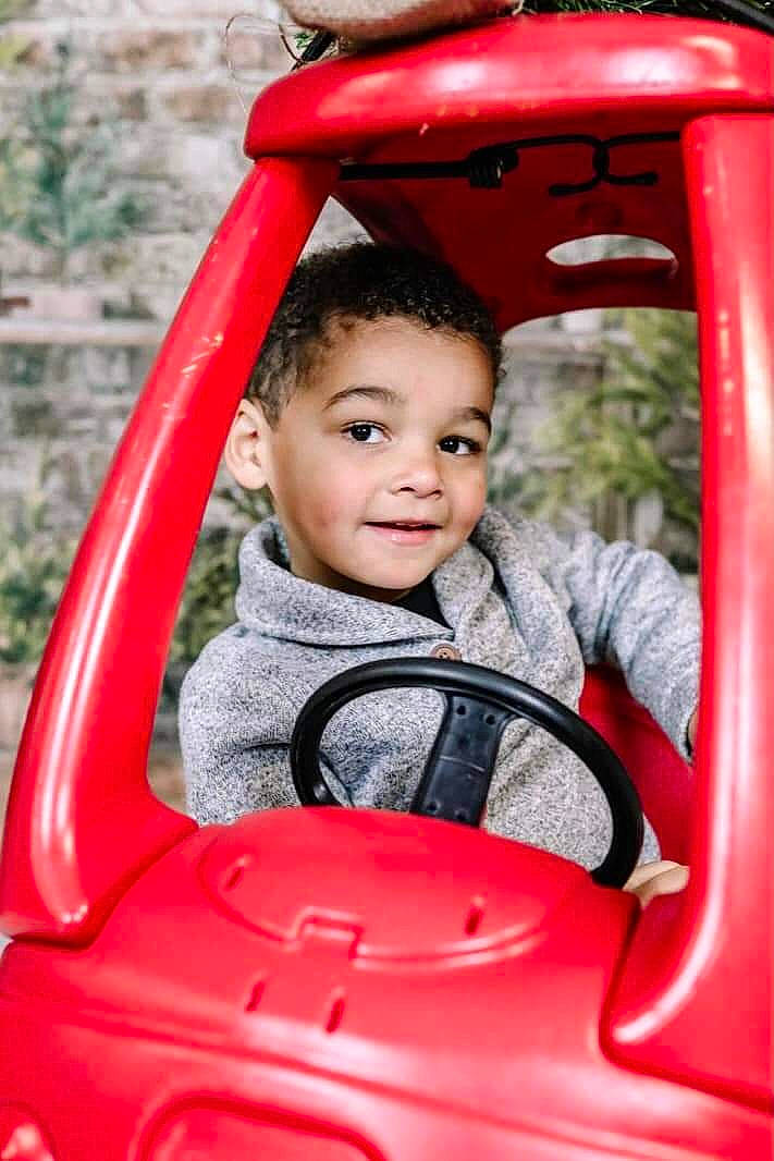 Graysen is registered to the contest to win money with this photo: automotive_design, automotive_exterior, automotive_mirror, eye, facial_expression, hand, happy, head, mode_of_transport, motor_vehicle, person, photograph, plant, product, public_space, red, skin, smile, steering_wheel, toddler