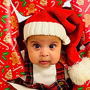 Eliza is registered to the contest to win money with this photo: baby, child, face, hat, santa_hat, christmas, wrapping_paper, holiday, plaid, clothing, festive, cute, indoors, portrait, closeup, red, white, expression, eyes, person