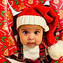 baby, child, face, hat, santa_hat, christmas, wrapping_paper, holiday, plaid, clothing, festive, cute, indoors, portrait, closeup, red, white, expression, eyes, person