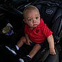 baby, child, car_seat, red_shirt, blue_eyes, infant, car_interior, seat_belt, black_shoes, white_socks, shorts, cute, young, portrait, sitting, vehicle, leather_seat, curious, indoors, casual_clothing