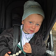 Gabriel participe au concours pour gagner de l'argent avec cette photo : baby_bib, blue_eyes, child, clothing, cute, expression, face, hand, hat, jacket, outdoor, person, rainy_day, rosy_cheeks, seatbelt, stroller, toddler, toy, transport, wheel