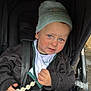 baby_bib, blue_eyes, child, clothing, cute, expression, face, hand, hat, jacket, outdoor, person, rainy_day, rosy_cheeks, seatbelt, stroller, toddler, toy, transport, wheel